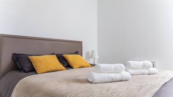 Un lit bien fait, recouvert d’une couverture beige, avec deux oreillers noirs et jaunes, et deux serviettes blanches pliées.
