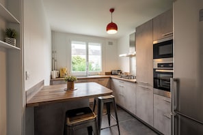 Une cuisine moderne avec un îlot central en bois, des appareils électroménagers en acier inoxydable et un luminaire suspendu rouge.