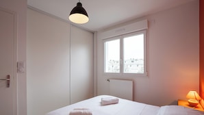 Une chambre d’hôtel avec un lit, deux serviettes, une fenêtre, un radiateur et une lampe.