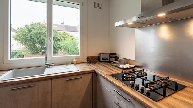Une cuisine moderne équipée d’une cuisinière en acier inoxydable, d’un évier et d’une fenêtre donnant sur un jardin.