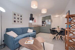 Un espacio habitable moderno con un sofá azul, una mesa de comedor de madera y una zona de cocina.