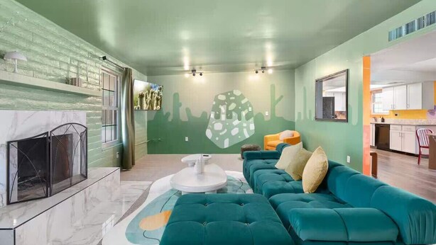 A modern living room with a teal sofa, a fireplace, and a green accent wall. - Relaxing 4BR with Pool, Game Room & BBQ Fun (Tucson)