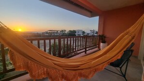 A hammock on a balcony with a view of the sunset and buildings in the distance. - Beachfront house with sunset views (São Miguel do Gostoso)