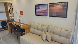 A cozy living area with a beige sofa, a wooden dining table with chairs, and two framed sunset pictures on the wall. - Beachfront house with sunset views (São Miguel do Gostoso)