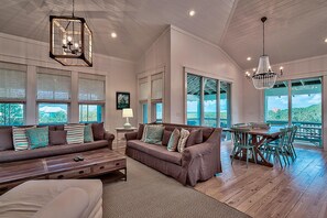 A spacious living room with a large sofa, a dining table with chairs, and a chandelier. - Sea Glass on 30A (Santa Rosa Beach)