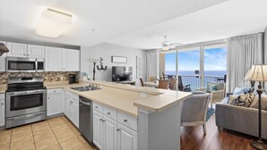 A modern kitchen with white cabinets, a large island, and a view of the ocean. - Majestic Beach Towers 1-1510 (Panama City Beach)