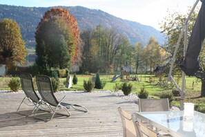 Eine Holzterrasse mit Stühlen und einem Tisch, ein Spielplatz und eine gebirgige Landschaft im Hintergrund.