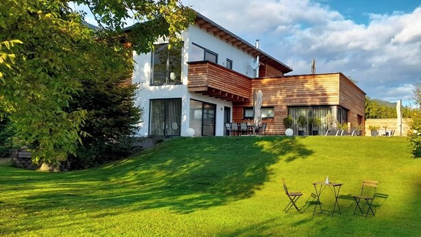 A modern two-story house with a sloped roof, large windows, and a well-maintained lawn. - Seeidylle Winkler vacation apartment directly on Lake Ossiach with its own bathing beach (Bodensdorf)