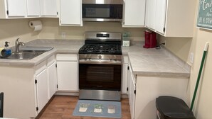 A compact kitchen with white cabinets, a stainless steel stove, a microwave, and a red coffee maker.