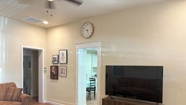A living room with a sofa, a coffee table, a TV on a wooden stand, a patterned rug, and a clock on the wall.