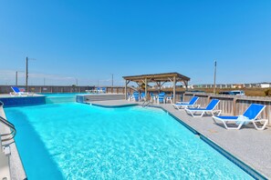 Una piscina azul cristalina con sillas de descanso azules y una pérgola de madera.