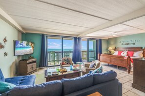 Ett vardagsrum med en stor TV, en soffa, ett soffbord och utsikt över havet.
