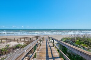 Un paseo marítimo de madera que conduce a una playa, con olas rompiendo sobre la orilla.