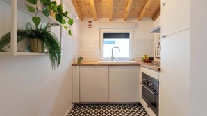 A compact kitchen with white cabinets, a wooden ceiling, a black and white patterned floor, and a window with a faucet. - Elegant Studio with Terrace & AC by HostWise (Porto)