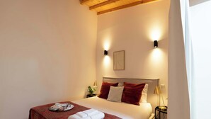 A neatly made bed with a red blanket and white pillows, a bedside table with a lamp, and a wall-mounted light fixture. - Elegant Studio with Terrace & AC by HostWise (Porto)