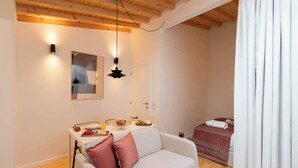 A cozy room with a wooden ceiling, a white sofa with a pink pillow, a dining table with breakfast items, and a bed with a red patterned bedspread. - Elegant Studio with Terrace & AC by HostWise (Porto)