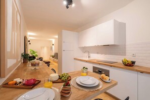 Eine moderne Küche mit weißen Schränken, einer Holzarbeitsplatte und Frühstücksangeboten wie Brot, Käse und Obst.