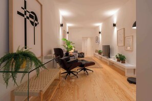 Ein modernes Wohnzimmer mit Holzboden, einer Couch, einem Couchtisch und einem Fernseher. An den Wänden befinden sich Pflanzen und gerahmte Bilder.