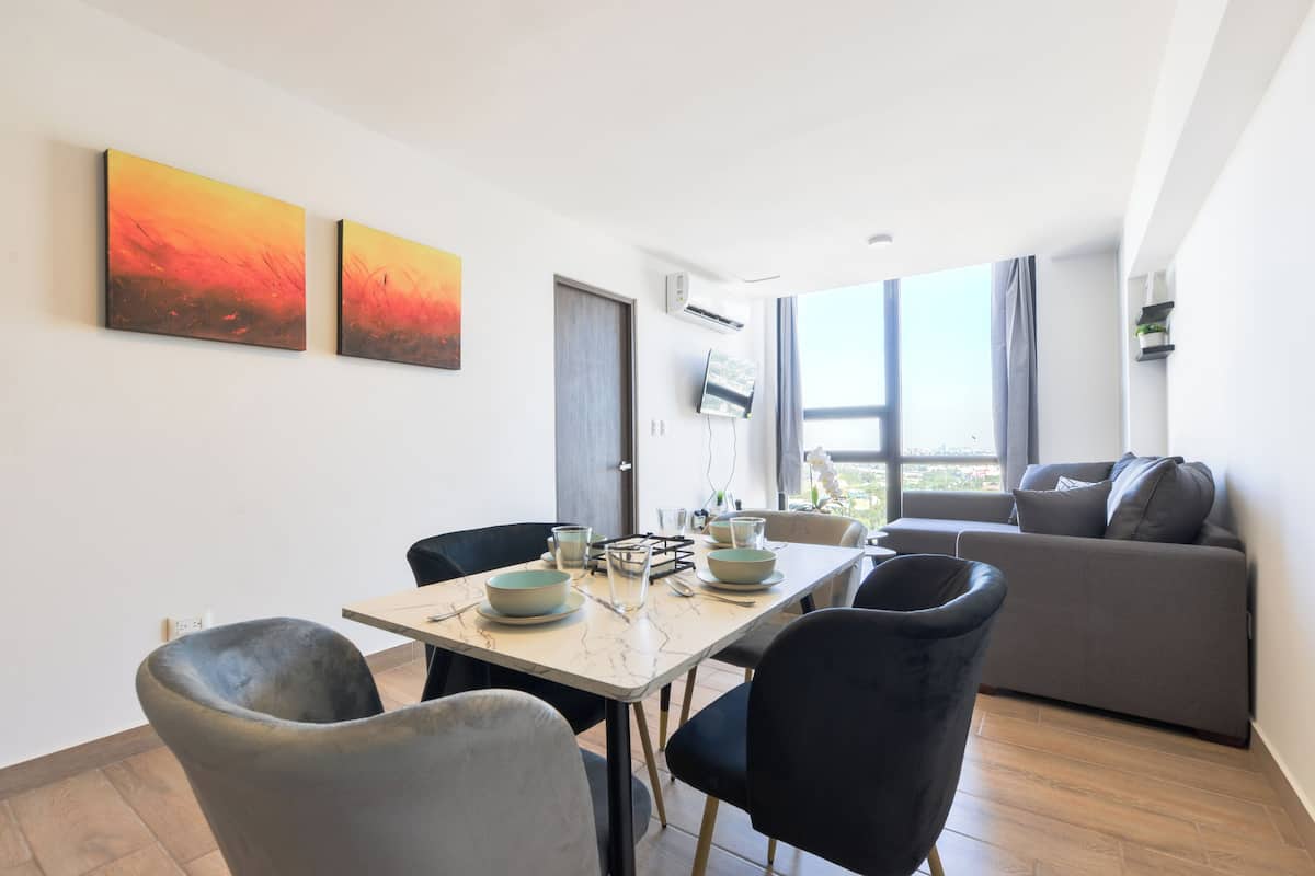 A modern living room with a dining area, large windows, and two abstract paintings on the wall.