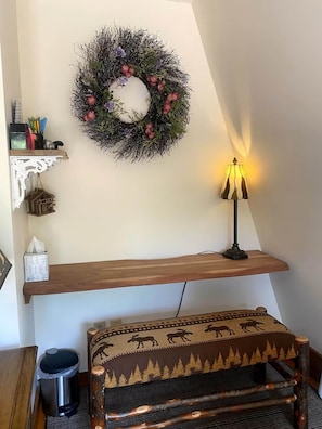 A room with a wooden bench, a wall-mounted shelf with a lamp, and a decorative wreath. - Lake Waukewan Camp in Meredith (Meredith)