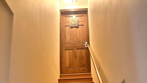Una escalera de madera con barandilla que lleva a una puerta con un cartel en la parte superior.