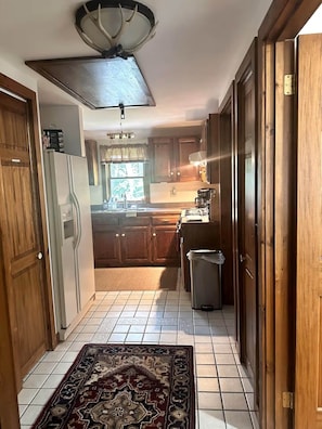 A kitchen with wooden cabinets, a refrigerator, a sink, and a trash can. - Lake Waukewan Camp in Meredith (Meredith)