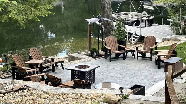 Un patio al aire libre con sillas Adirondack, una chimenea y un muelle que se adentra en un lago.