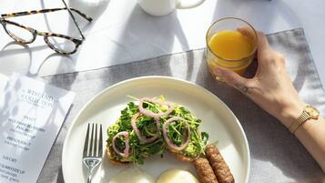 Een ontbijttafel met eten op een bord, een koffiekop, een glas sinaasappelsap en een cafetière.