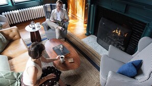 A cozy living room with a fireplace, a sofa, a coffee table, and a person reading a book.