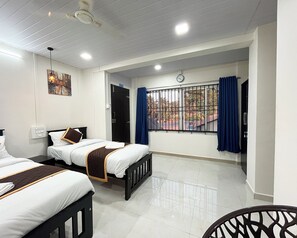 A hotel room with two beds, a window with metal bars, a clock, and a ceiling fan. - Panduranga Elite (Honavar)