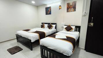 A hotel room with two beds, each with a white and brown bedspread, a black headboard, and a small bedside table. There is a door on the right and a wall-mounted light fixture above the beds.