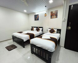 A hotel room with two beds, each with a white and brown bedspread, a black headboard, and a small bedside table. There is a door on the right and a wall-mounted light fixture above the beds.