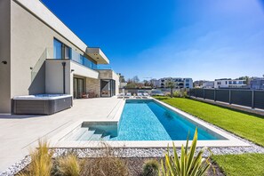 Ein modernes Haus mit Swimmingpool, Whirlpool und gepflegtem Rasen.