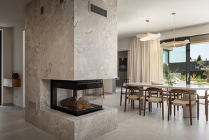 Ein modernes Wohnzimmer mit Kamin, Essbereich und großen Fenstern.