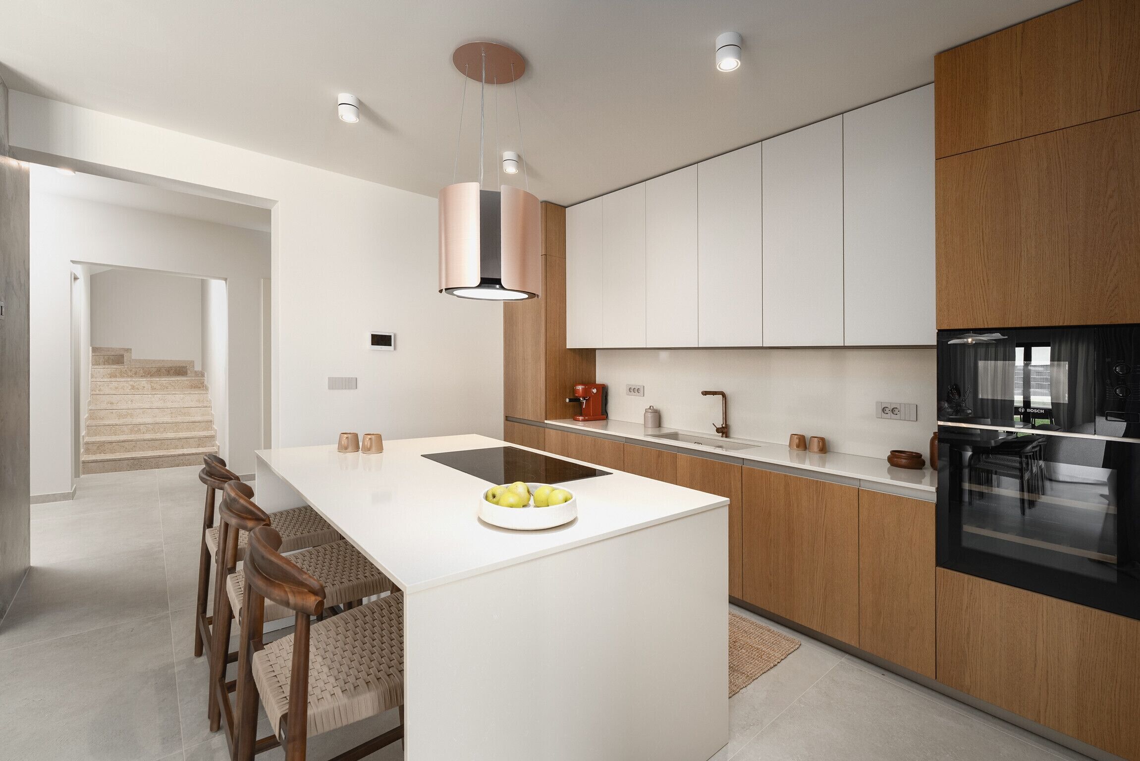 A modern kitchen with a central island, wooden cabinets, a built-in oven, and a dining area with chairs.