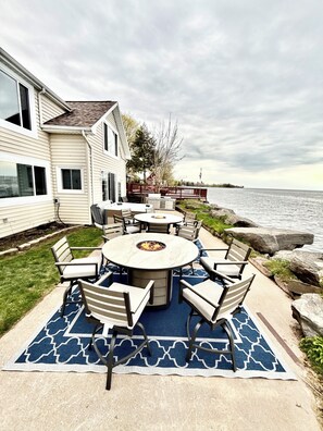 A patio with a round table and chairs, a fire pit, and a view of the water. - Lakeside Zen Spa Retreat - Sauna, Jacuzzi, Massage Chairs, Red Light Therapy (Hilton)