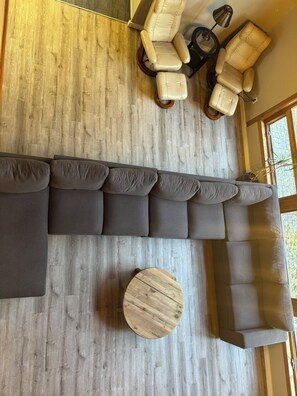 Un salon moderne avec un canapé d’angle, deux fauteuils inclinables, une table basse ronde et un plancher en bois.