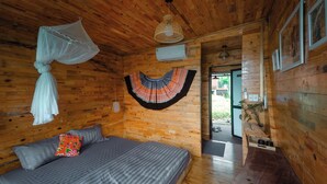 A wooden cabin bedroom with a bed, mosquito net, air conditioning unit, and a hanging decorative item. - Ecolodge Cat Ba (Hai Phong)