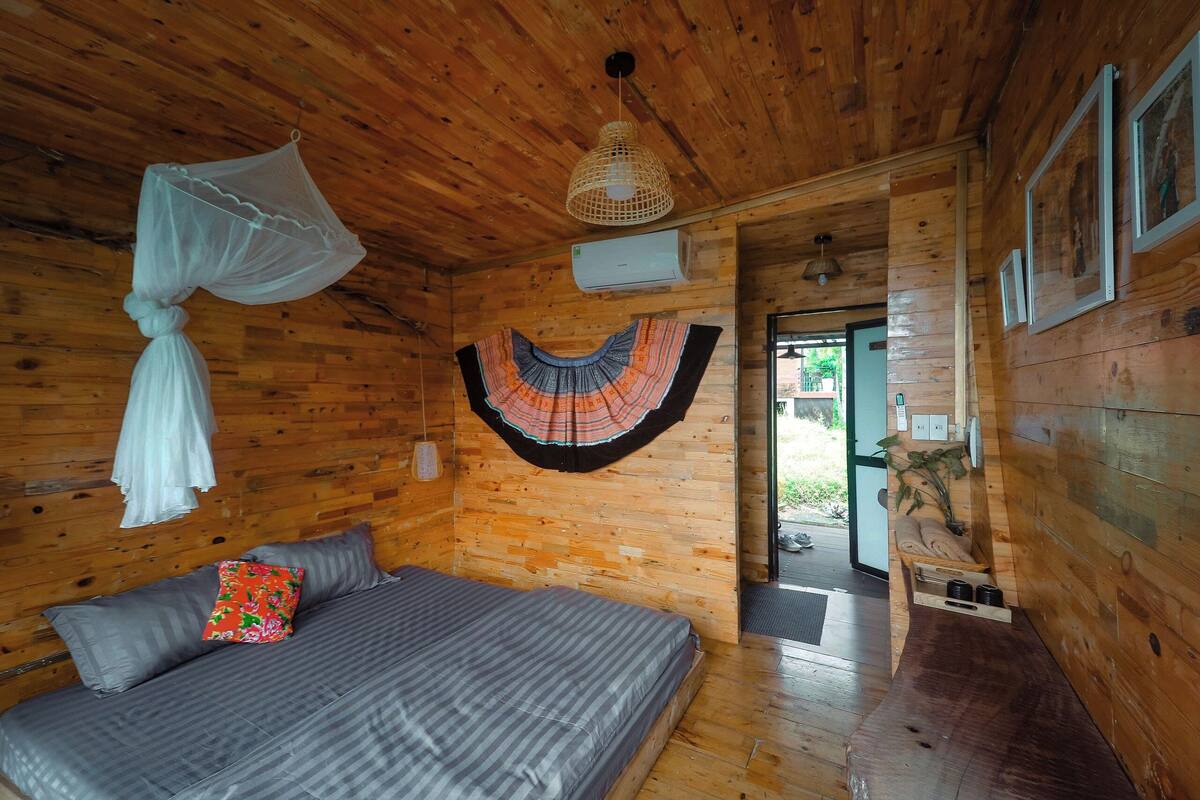 Ein Schlafzimmer einer Holzhütte mit Bett, Moskitonetz, Klimaanlage und einem hängenden Dekorationsobjekt.
