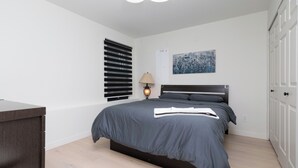 Un dormitorio moderno con cama, escritorio, lámpara y un cuadro en la pared.
