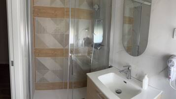 Ein modernes Badezimmer mit Duschkabine aus Glas, Waschbecken mit Handtrockner und Holzschrank.