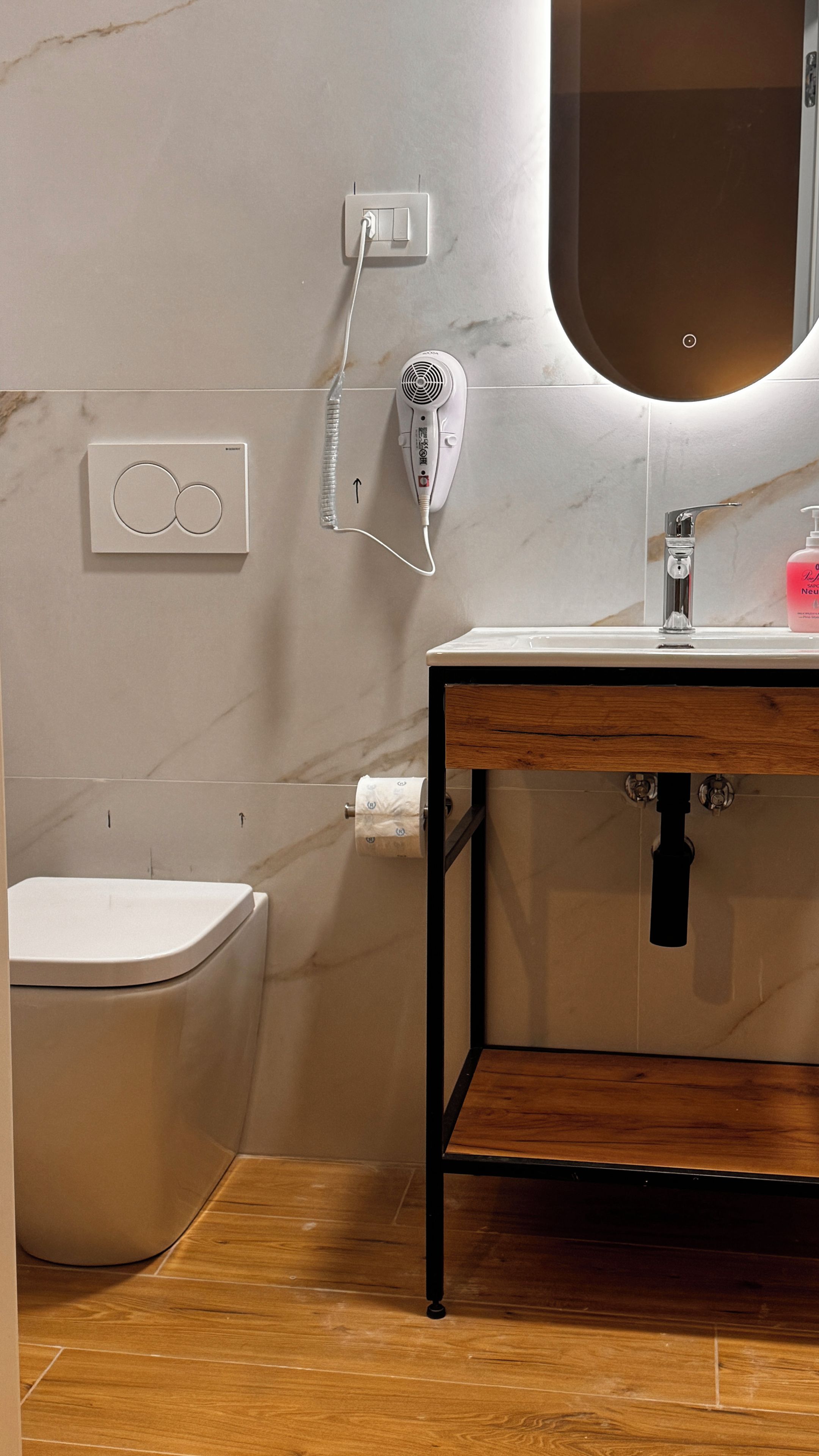 Ein Badezimmer mit Toilette, Waschbecken mit Spiegel und einem Fön an der Wand.