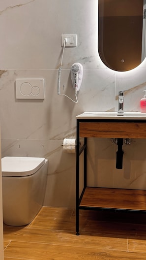 Ein Badezimmer mit Toilette, Waschbecken mit Spiegel und einem Fön an der Wand.