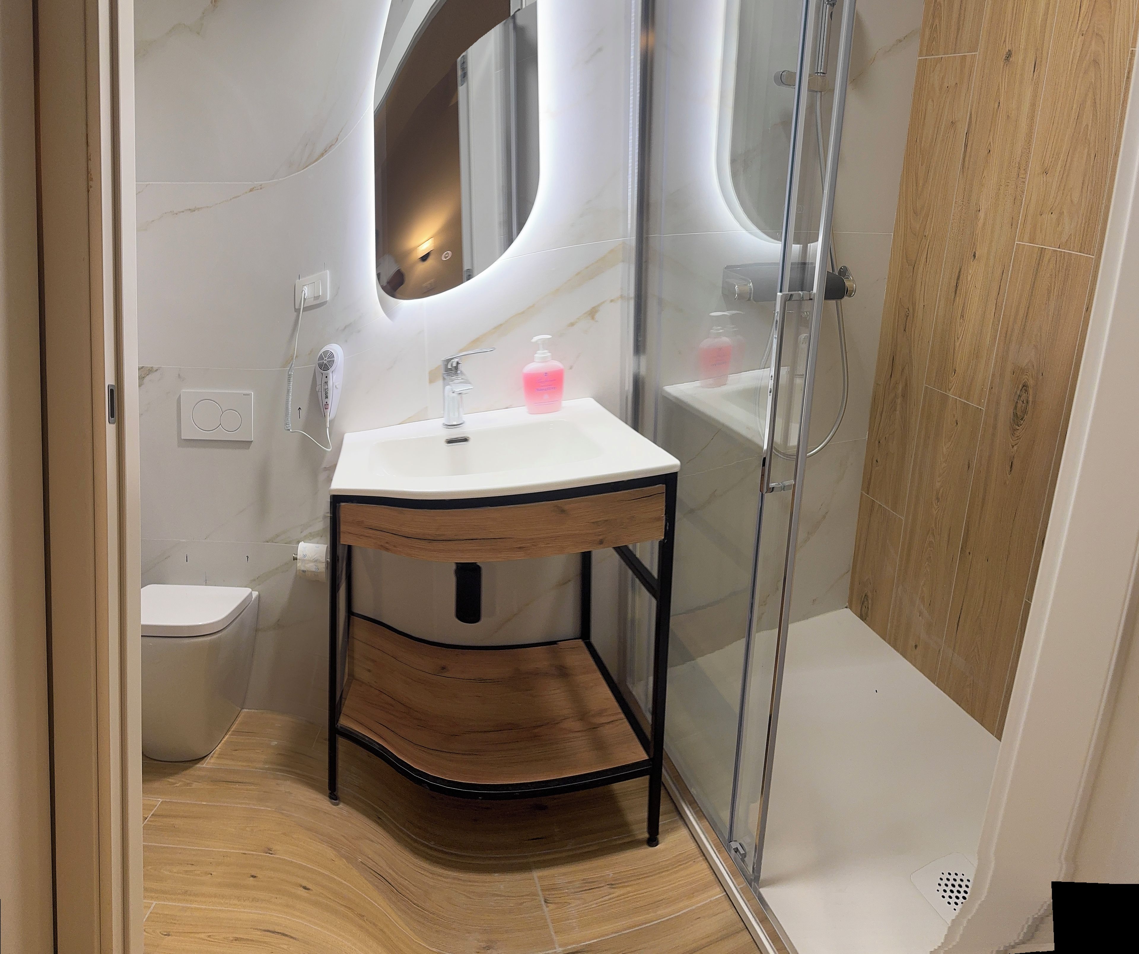 Un baño con lavamanos blanco, tocador de madera y cabina de ducha de vidrio.
