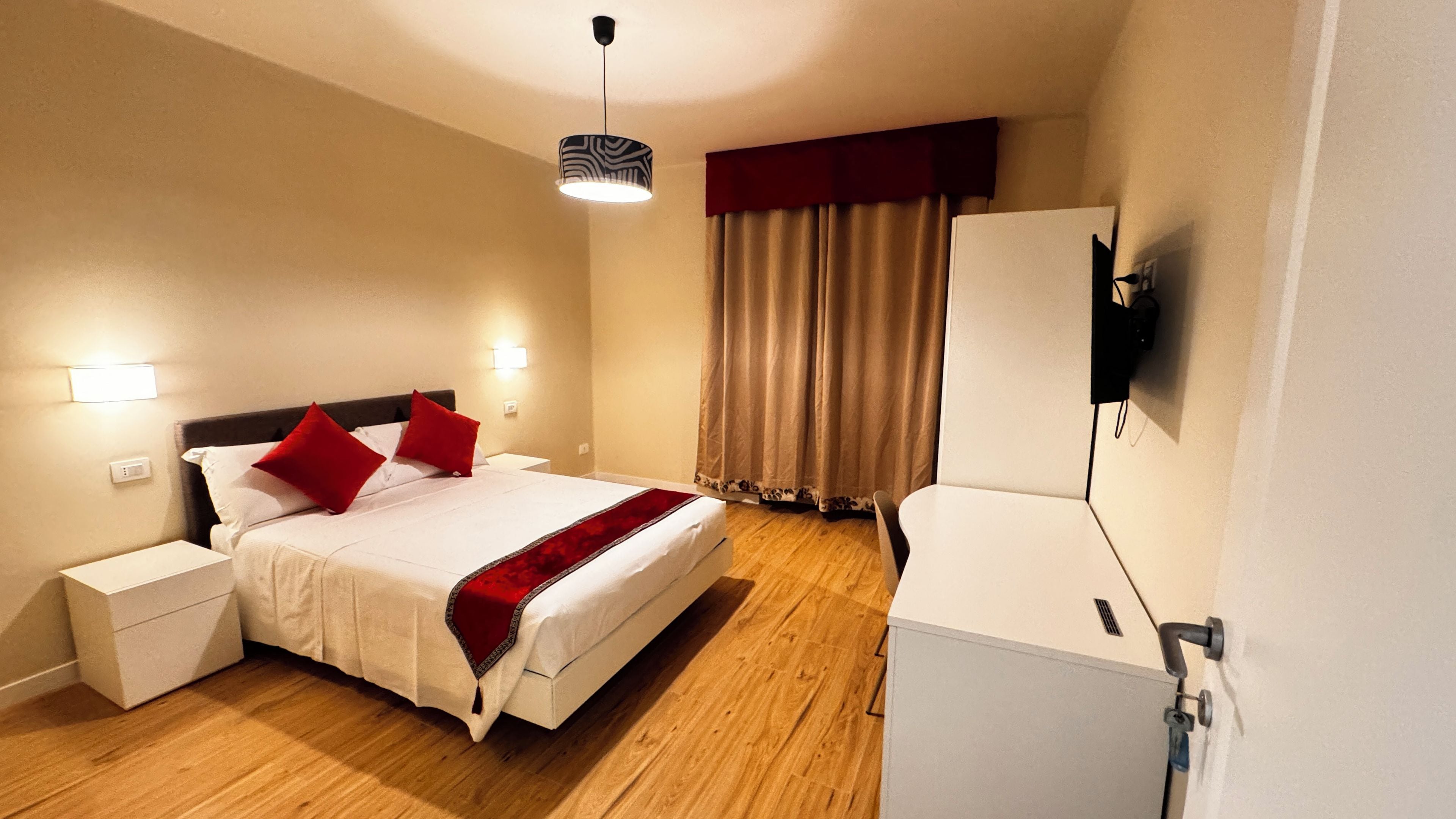 A hotel room with a bed, bedside tables, a TV, and a window with curtains.