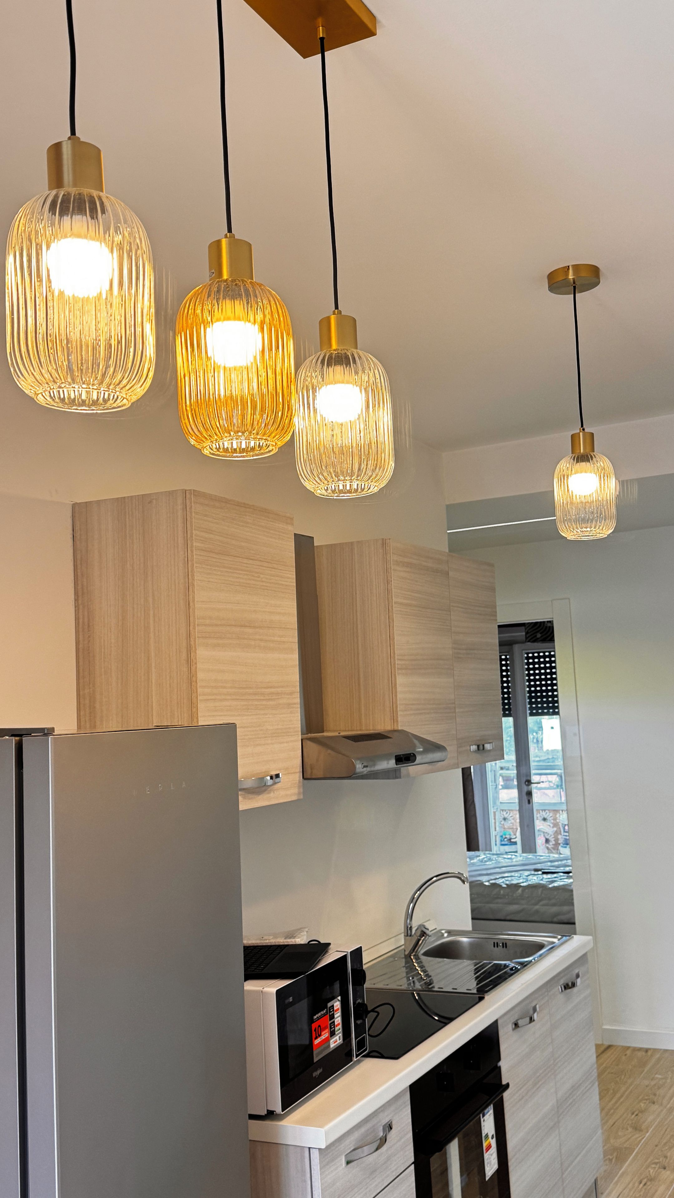 Una cocina moderna con refrigerador, microondas y estufa, con lámparas colgantes de diseño único.