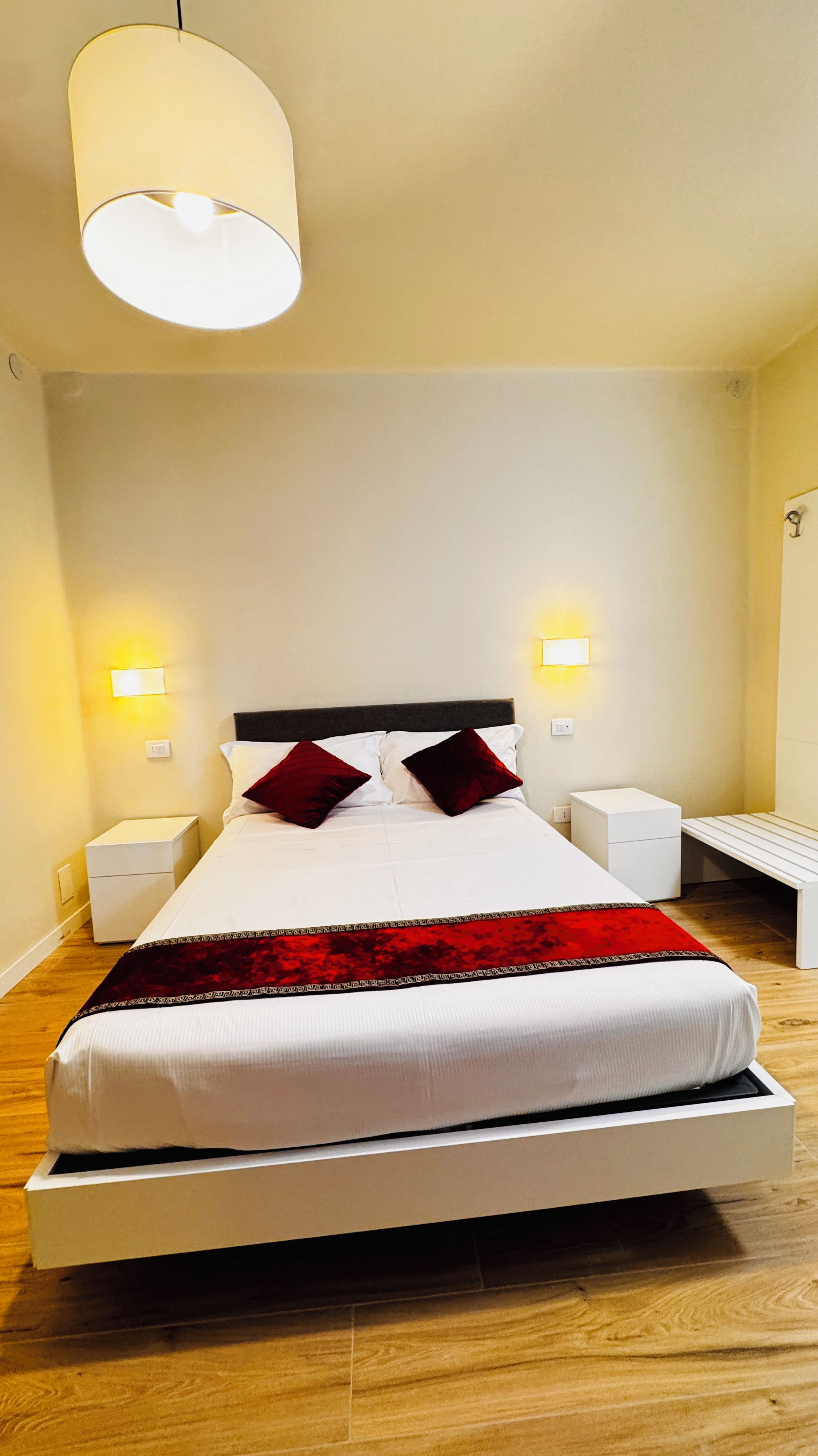 A neatly made bed with a white and red bedspread, two bedside tables with lamps, and a hanging light fixture.