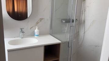 A bathroom with a marble-tiled wall, a white sink with a mirror, a glass-enclosed shower, and wooden storage.