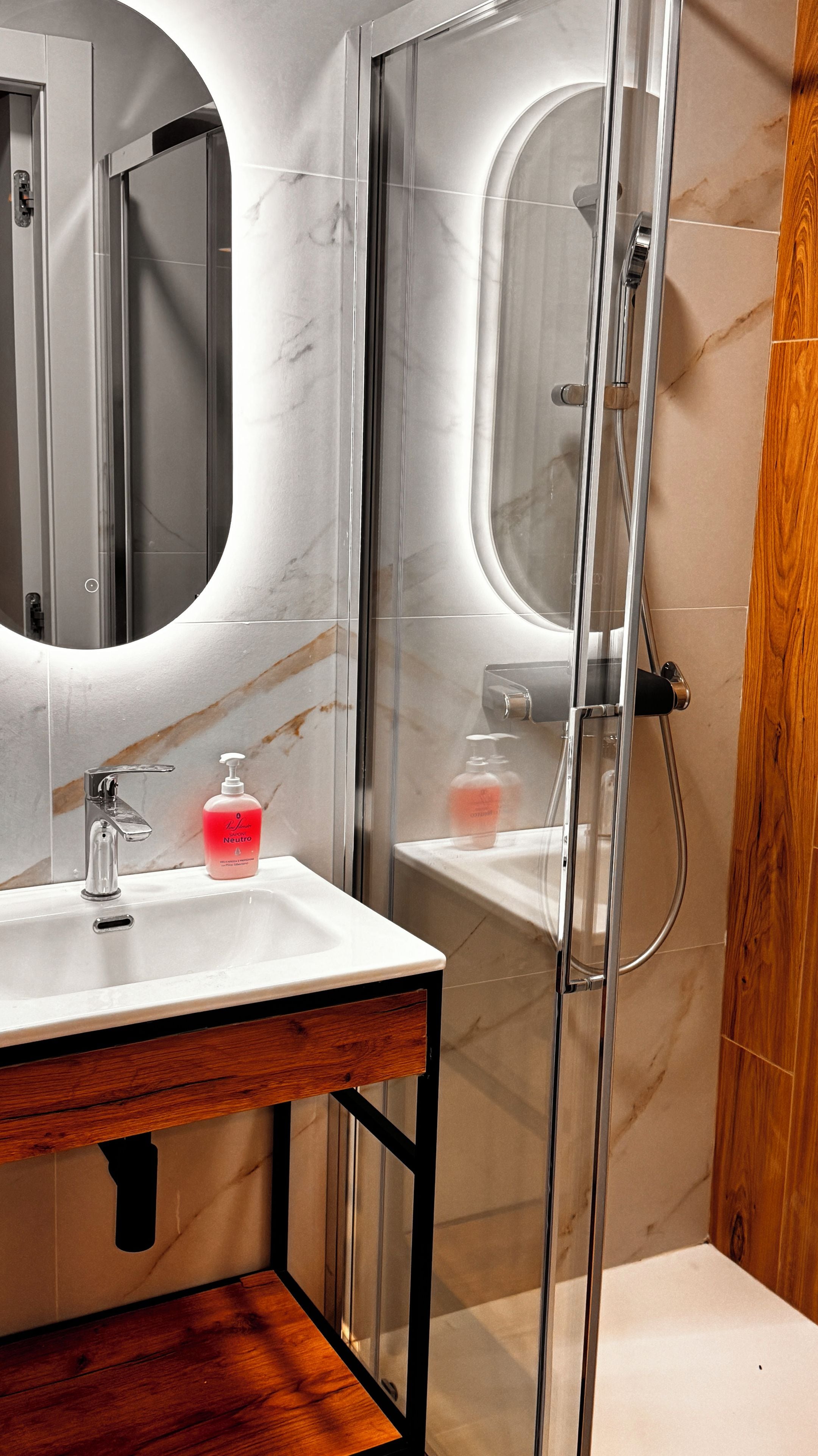 Un baño moderno con tocador de mármol, cabina de ducha con vidrio y detalles de madera.