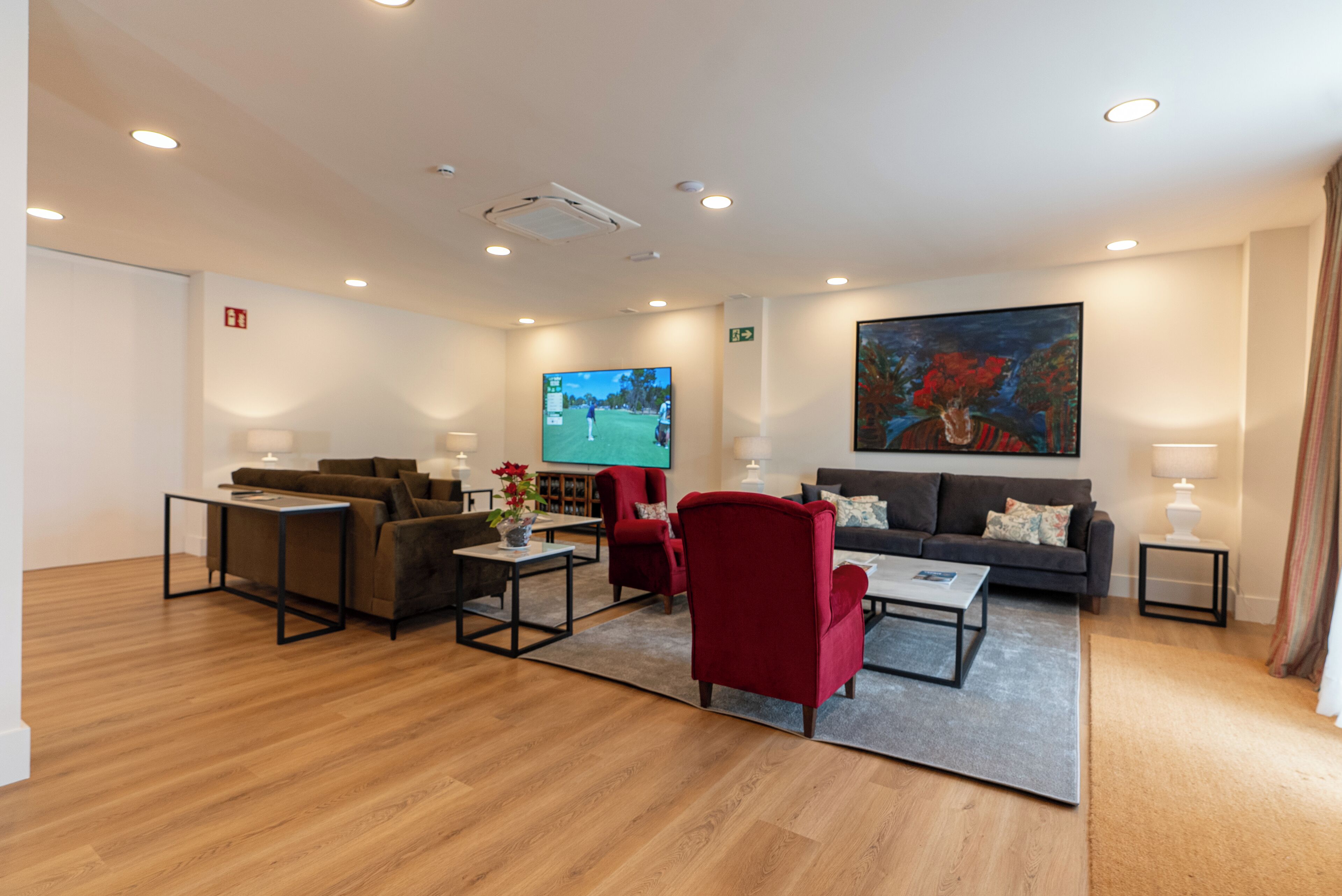 A modern living room with a flat-screen TV, sofas, a red armchair, and a coffee table.